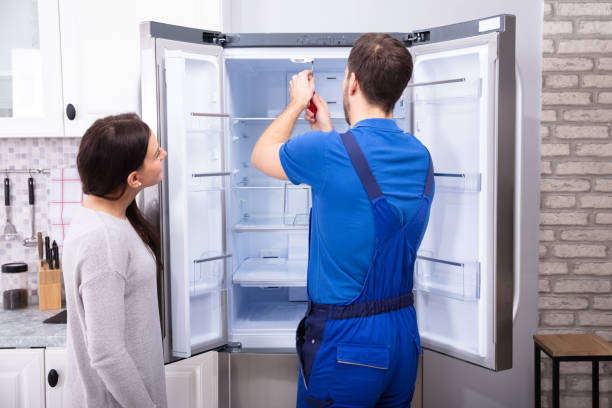 woman looking at male repairman fixing refrigerator with screwdriver